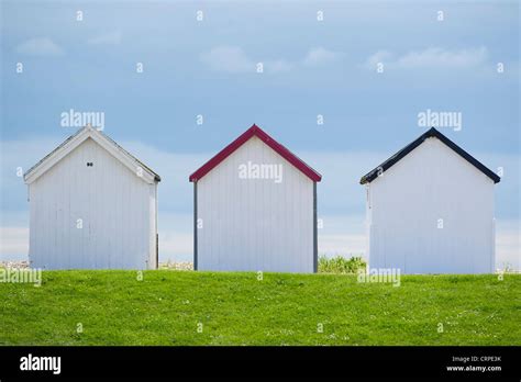Three English Beach Huts Sitting Between The Beach And A Grass Hill