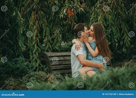Beautiful Couple In Love Sits In A Park On A Bench In The Summer Hugs
