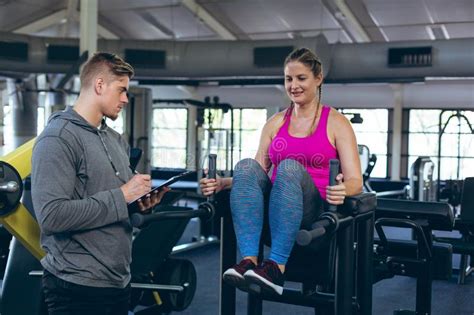 Trainer Assisting Female Athlete With Exercise In Fitness Studio Stock