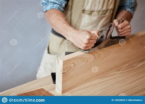 Carpenter Working With Wood Using Plane Against White Wall In Studio