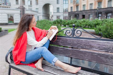 Attractive Girl Sitting On A Bench With Bare Feet Covered With A Red Blanket In The New
