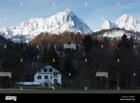 A Traditional Bavarian House In The Alps Is Dwarfed By A Snow Capped
