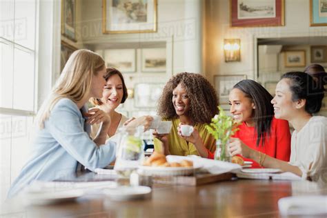 Smiling Women Drinking Coffee And Talking At Restaurant