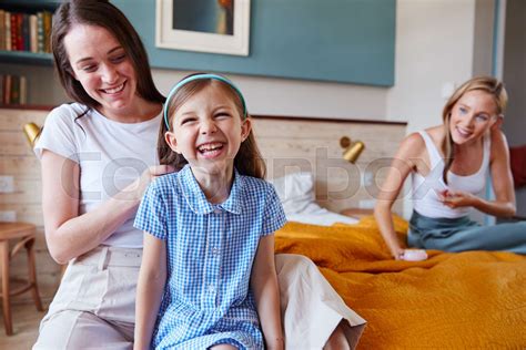 Same Sex Female Couple At Home Getting Daughter Ready For School Plaiting Her Hair Stock Image