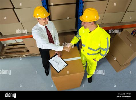 Smiling Warehouse Manager And Worker Shaking Hands In Warehouse Stock