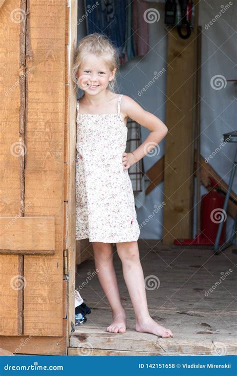 Barefoot Girl In A Summer Sundress Stands In The Doorway Of The Shed