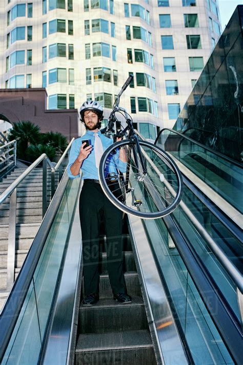 Caucasian Businessman Carrying Bicycle On Escalator Stock Photo