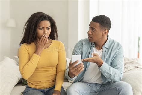 Sad Millennial African American Husband With Smartphone Scolding Offended Confused Wife Stock