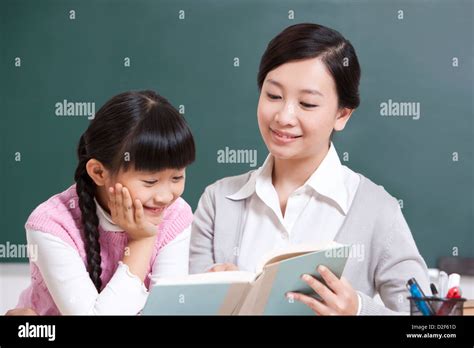 Happy Teacher And Schoolgirl Reading A Book In Classroom Stock Photo
