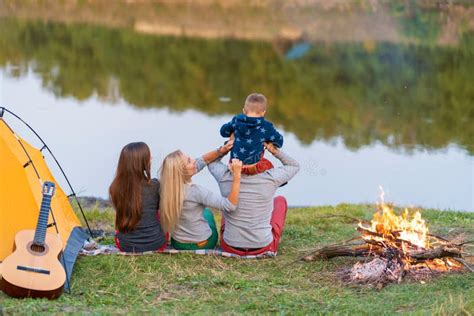 A Group Of Friends Is Enjoying View Camping With Bonfire On Riverside