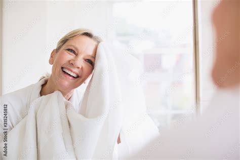 Smiling Mature Woman Drying Face With Towel At Bathroom Mirror Stock