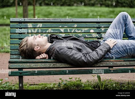 Handsome Blond Young Man Laying On Green Wooden Park Bench Thinking