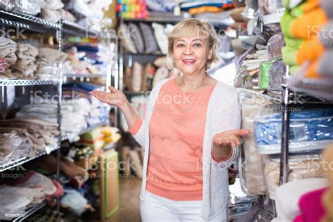 Positive Mature Woman Standing Among Shelf In The Textile Shop Stock