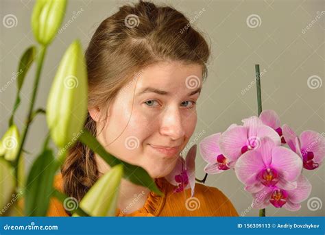 A Beautiful Girl With An Orchid In Her Hands Enjoys The Smell Of