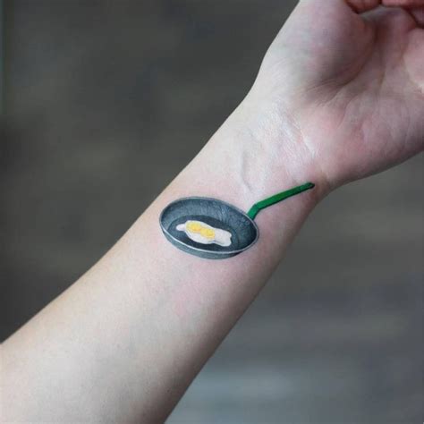 Small Hyper Realistic Omelet And Frying Pan Tattoo On The Inner Wrist