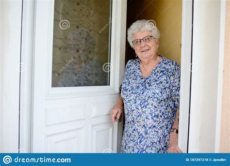Elderly Senior Woman Opening Front Door Of House And Welcoming People