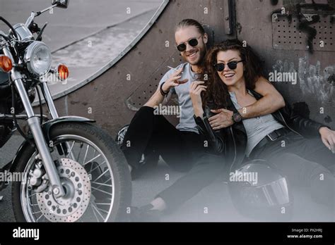 Smiling Couple Of Bikers Embracing And Smoking On Asphalt With Chopper
