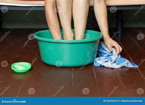 Girl Washes Her Feet In A Bowl Of Water On The Wooden Floor At Home