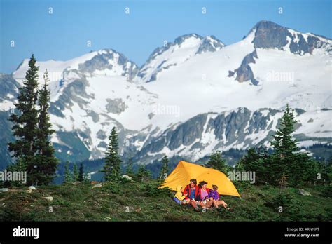 Young Couple Camps In Meadow With Mountain Backdrop In Whistler Alpine