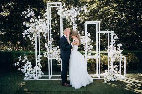 A Bride And Groom Standing In Front Of An Outdoor Wedding Ceremony Arch