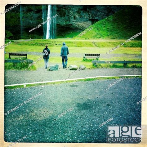 Couple Walking Towards Seljalandsfoss Waterfall Iceland Stock Photo