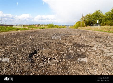 Damaged Rural Road Cracked Asphalt Blacktop With Potholes And Patches