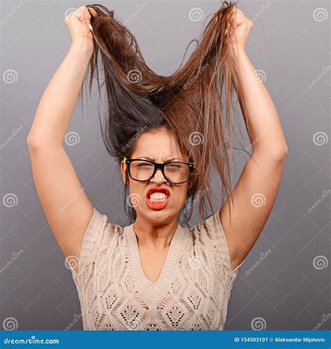 Portrait Of A Hysterical Woman Pulling Hair Out Against Gray Background
