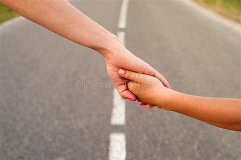 Mother And Child Hold Hands Together While Walking Along The Highway In