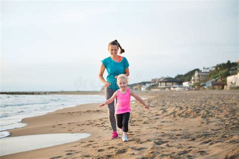 Fit Happy Mother Running Behind Young Daughter On The Beach Stock