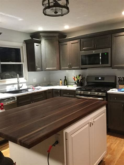 A white torano marble design with varying sizes of grey veining and hints of warm taupe, creating a chunky marble effect in shades of grey that display intricate depth and detail. West Point grey cabinets. Walnut butcher block. Etched ...