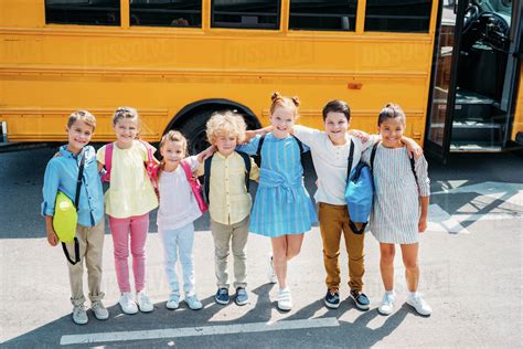Group Of Adorable Schoolchildren Standing In Front Of School Bus And