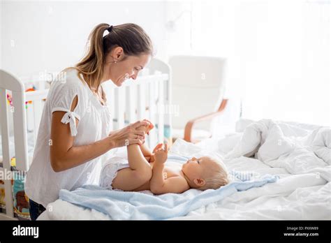 Young Mom Changing Baby Diaper After Bath In Sunny Bedroom Stock Photo