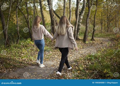 The Girls Are Holding Hands Friends Are Walking In The Autumn Forest