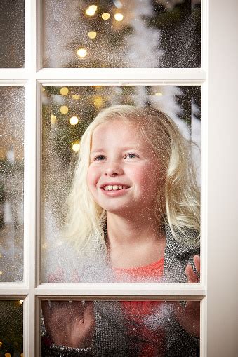 Girl Looking Through Snowy Window At Christmas Stock Photo Download