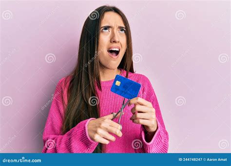 Young Hispanic Girl Cutting Credit Card Using Scissors Angry And Mad