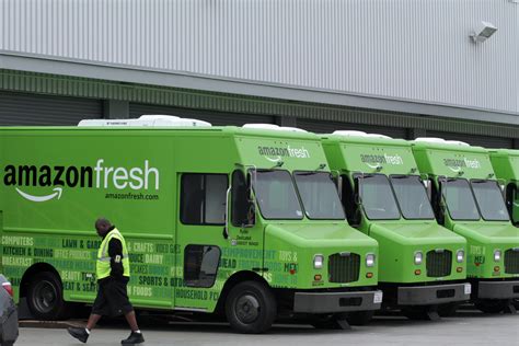 A Worker Walks Past Amazon Fresh Delivery Vans Parked At An Amazon