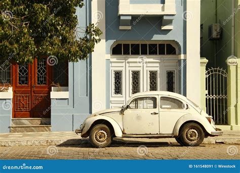 Horizontal Shot Of A Small Vintage White Car Parked In Front Of A Blue