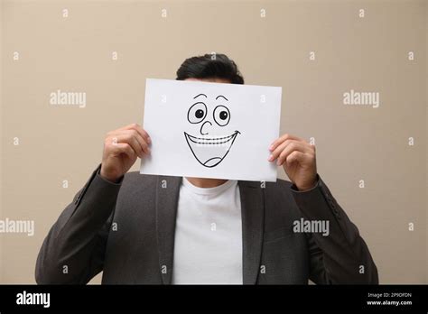 Man Hiding Emotions Using Card With Drawn Smiling Face On Beige
