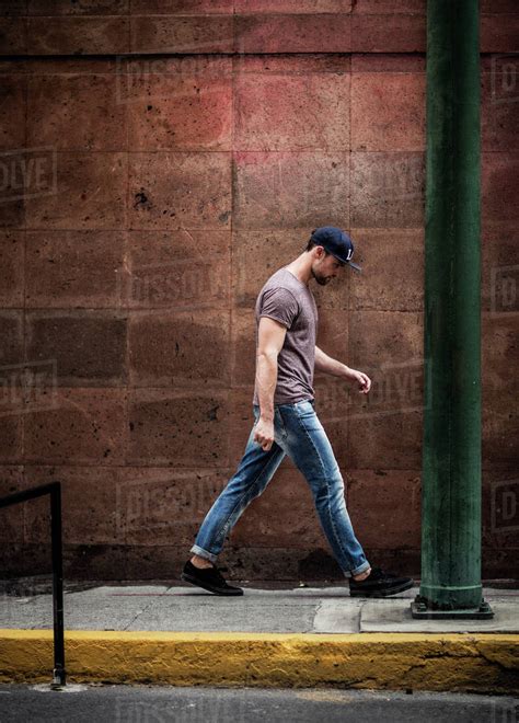 A man walking along a sidewalk alongside a wall. - Stock Photo - Dissolve
