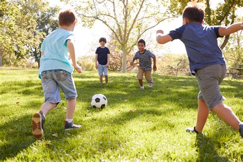 Four Young Schoolboys Playing Football Together In The Park The