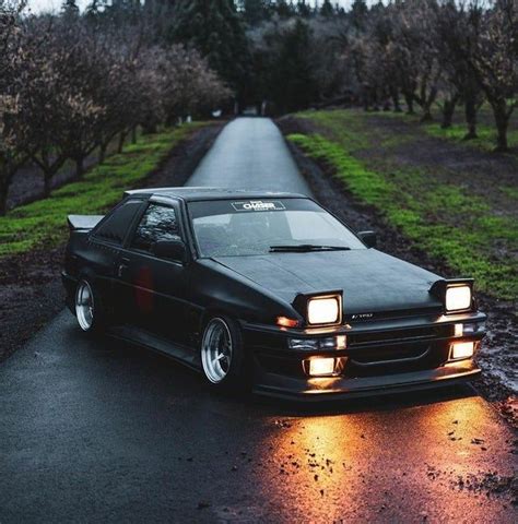 A Black Car Parked On The Side Of A Road Next To Some Grass And Trees