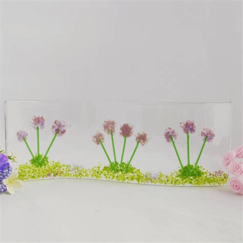 Three Flowers In A Clear Vase On A White Surface With Pink And Purple Flowers Next To It
