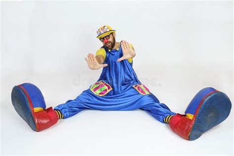 A Clown In A Bright Costume Sits With His Legs Apart And Put His Hands Forward Palms Stock