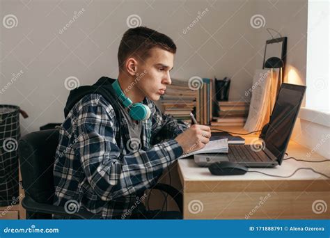 Teenage Boy Doing Homework Using Computer Sitting By Desk In Room Alone