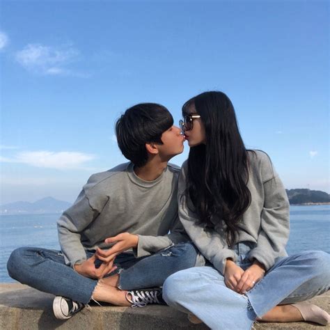 Two People Sitting On A Stone Wall Near The Ocean Kissing Each Other