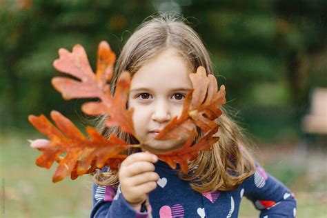 Cute Young Girl Holding Up A Branch With Leaves To Her Face By