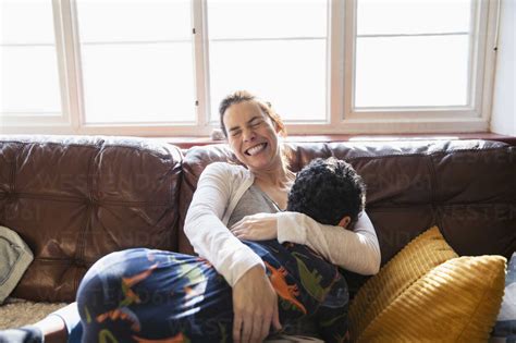 Happy Carefree Mother Cuddling With Son On Living Room Sofa