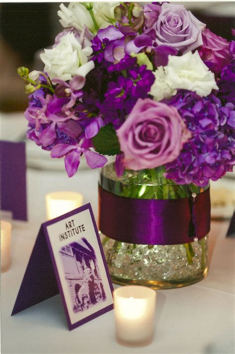 a vase filled with purple and white flowers on top of a table next to candles