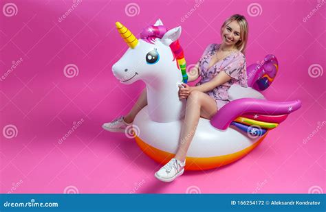 A Beautiful Blonde Girl In A Sundress With Slim Legs In White Sneakers Sits On An Inflatable