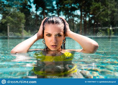 Woman In Swimming Suit With Hands On Head Posing In Pool On Resort